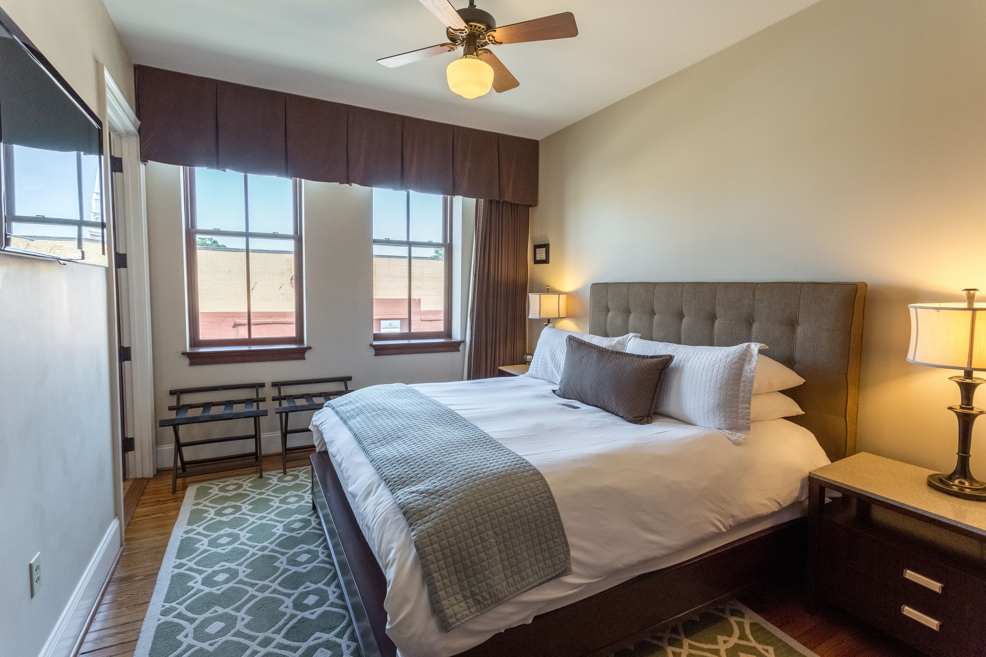 A hotel room with a large bed, two bedside lamps, a ceiling fan, and a view of the outside.