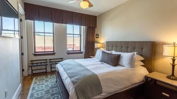 A hotel room with a large bed, two bedside lamps, a ceiling fan, and a view of the outside.