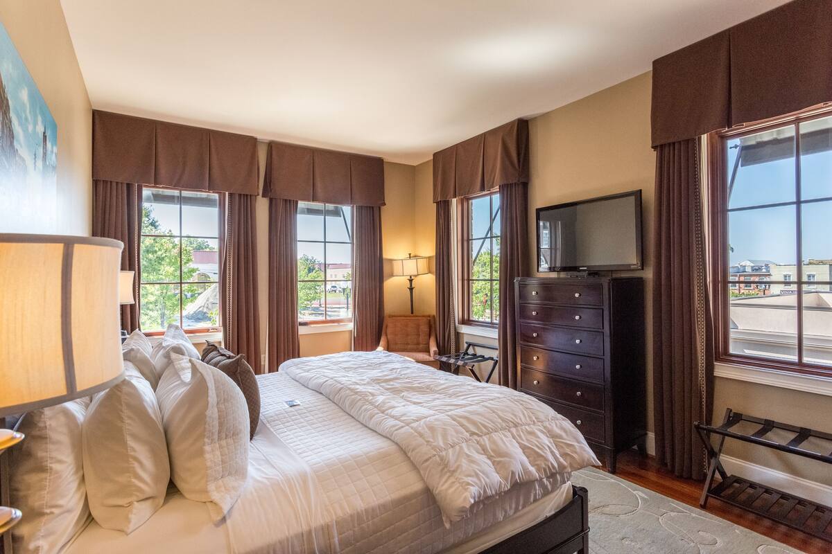 A hotel room with a large bed, a dresser, a television, and a window with curtains.