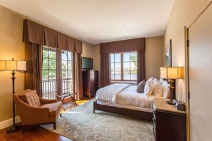 A hotel room with a bed, a chair, a desk, a television, and large windows.
