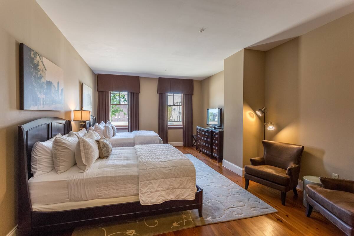 A bedroom with two beds, a dresser, a chair, and a TV.