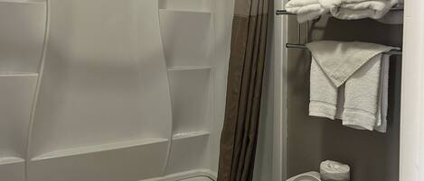 A bathroom with a bathtub, a toilet, and a towel rack with folded towels.