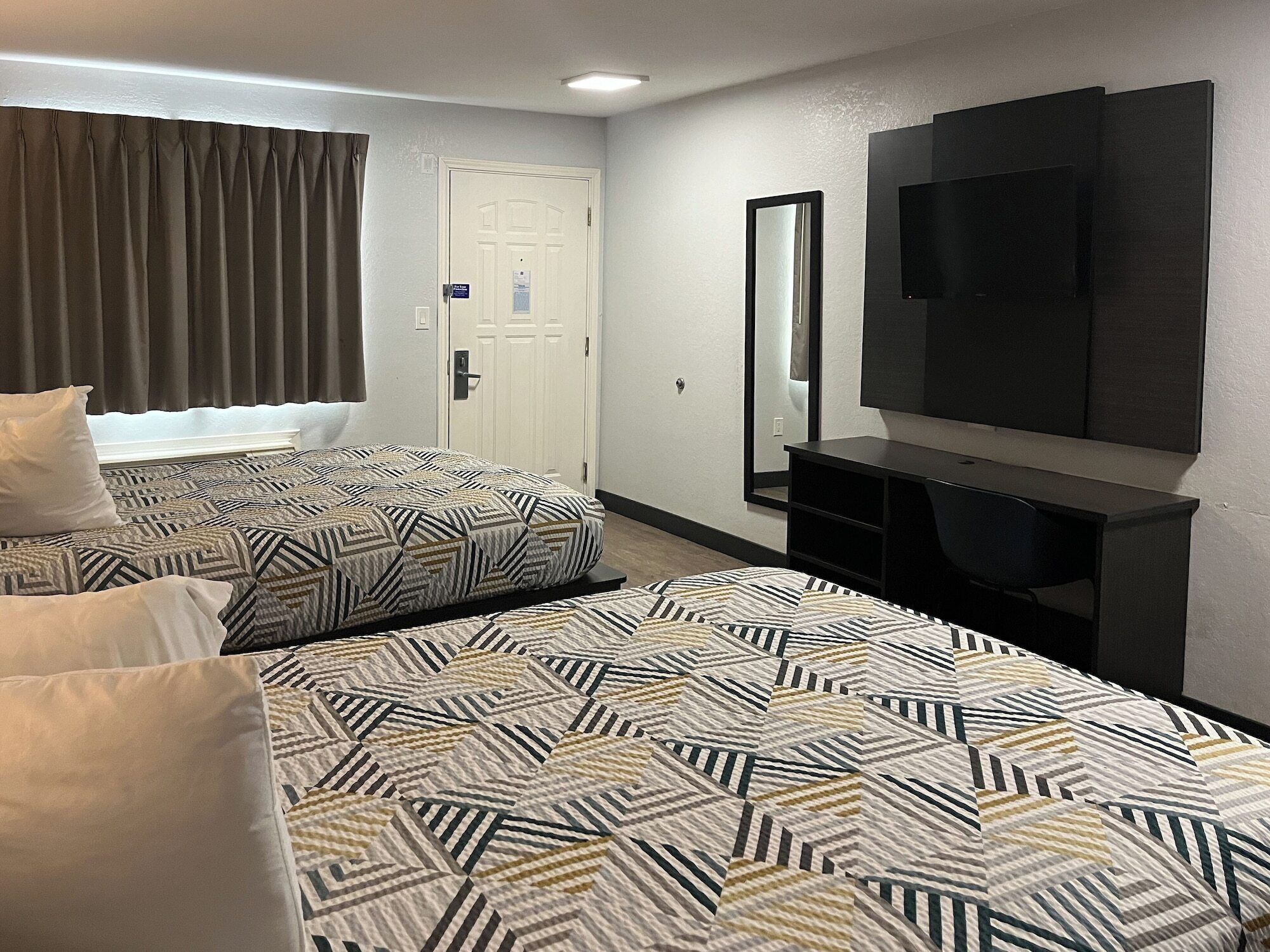 A hotel room with two beds, a TV, a mirror, and a door.