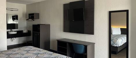 A modern hotel room with a bed, a desk, a chair, a mirror, and a wardrobe.