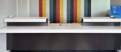 A reception area with a modern design, featuring a long counter, a colorful striped wall, and a digital screen displaying information.