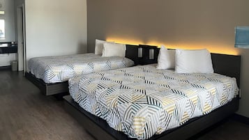 A modern hotel room with two beds, a dark headboard, and a small bathroom visible in the background.