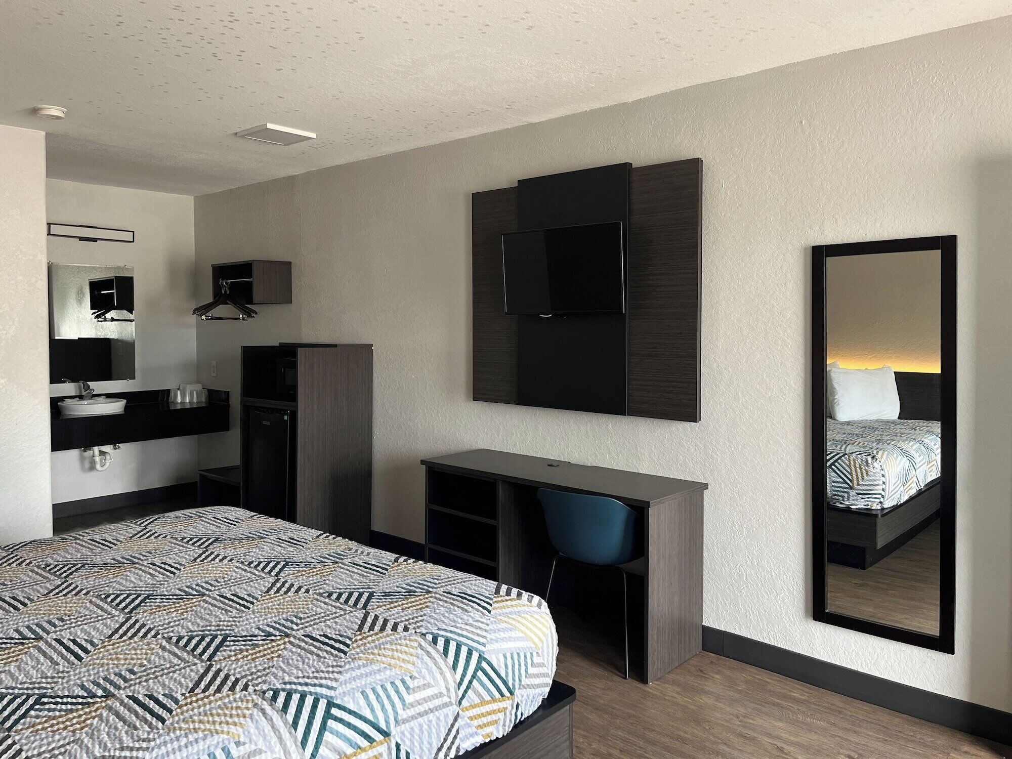 Une chambre d’hôtel moderne équipée d’un lit, d’un bureau, d’une chaise, d’une télévision et d’un miroir.