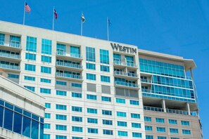 A modern hotel building with multiple floors, large windows, and flags on top. - The Westin Houston, Memorial City (Houston)