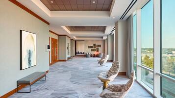 A modern hotel lobby with a long corridor, seating area, and large windows offering a city view.