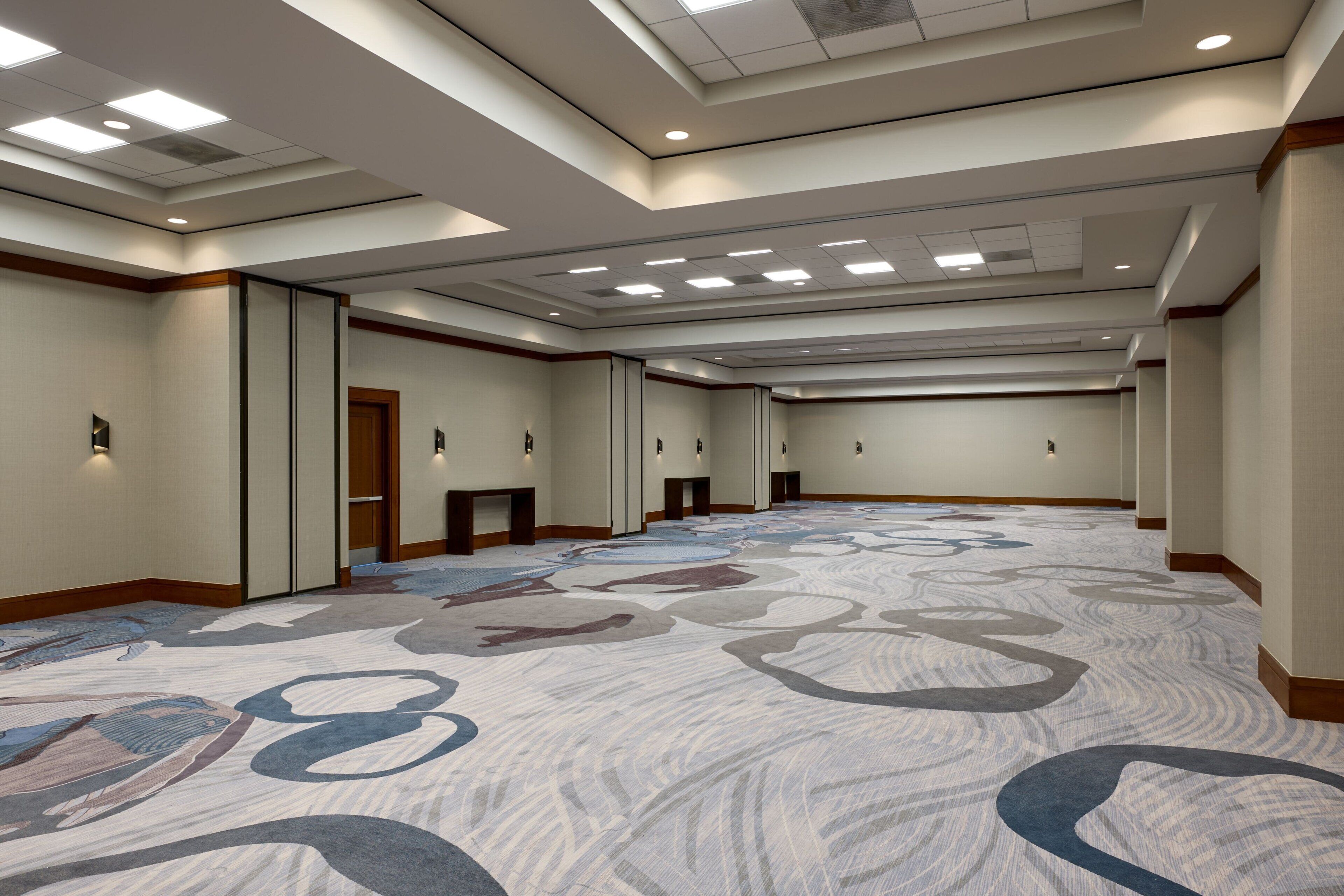 Un vaste couloir d’hôtel, agrémenté d’un tapis à motifs, d’un éclairage encastré et d’un design de plafond moderne.