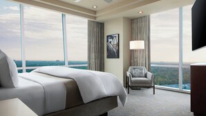 Ett hotellrum med en stor säng, en stol, ett skrivbord och utsikt över staden.