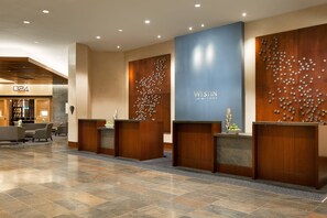 A hotel reception area with a modern design, featuring a large blue wall with the hotel name, wooden reception desks, and a seating area with chairs. - The Westin Houston, Memorial City (Houston)