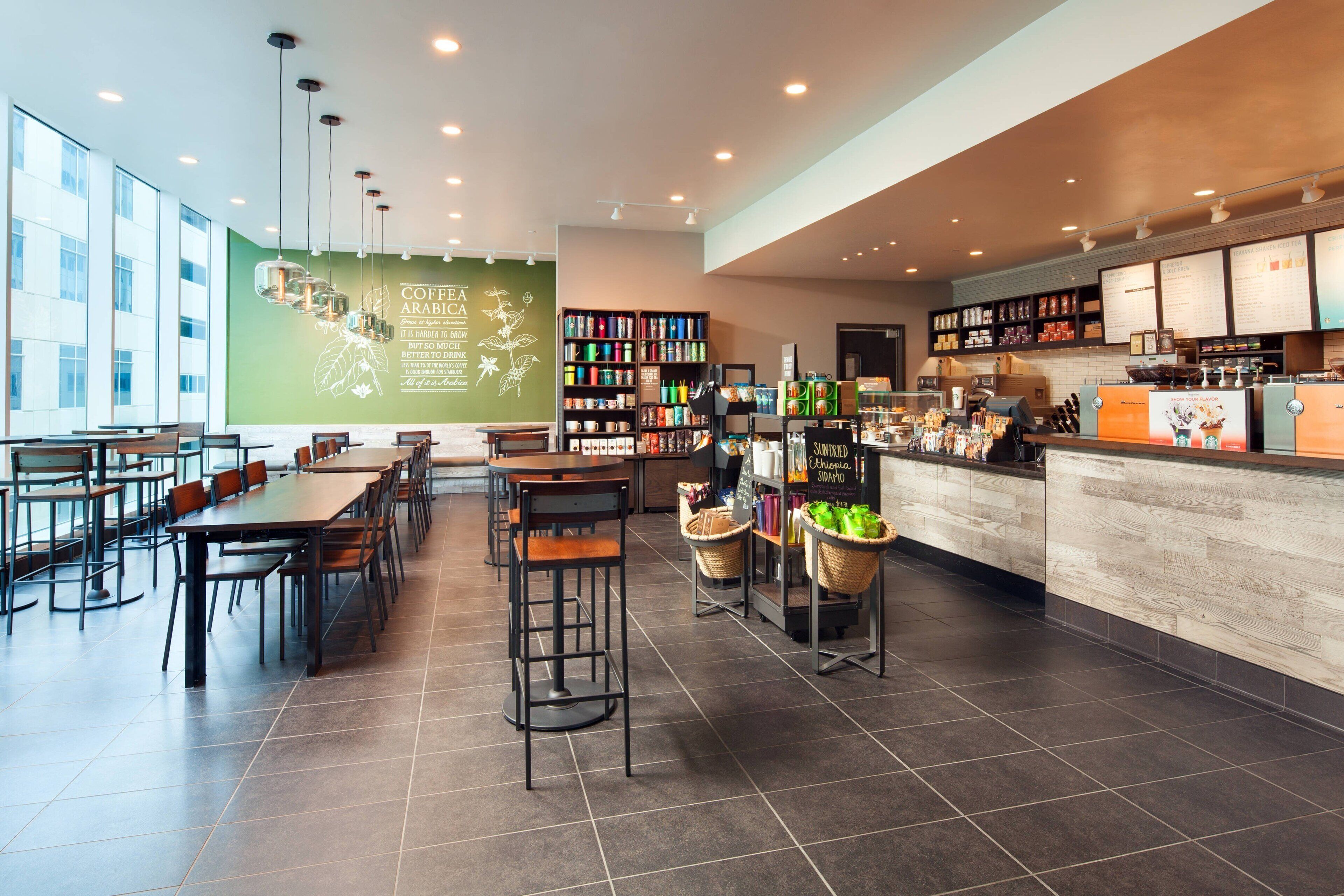 A modern coffee shop with a long counter, bar stools, and a seating area with tables and chairs.