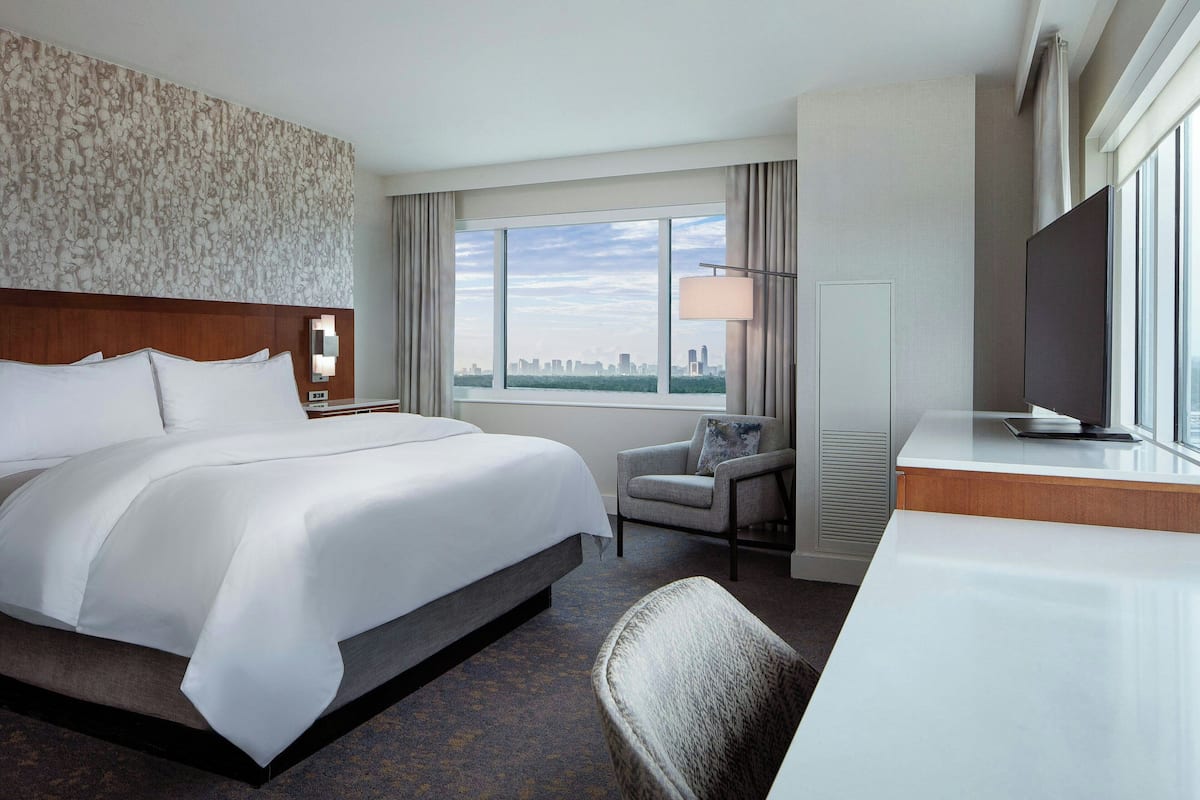 A hotel room with a large bed, a desk, a chair, a TV, and a window with a city view.