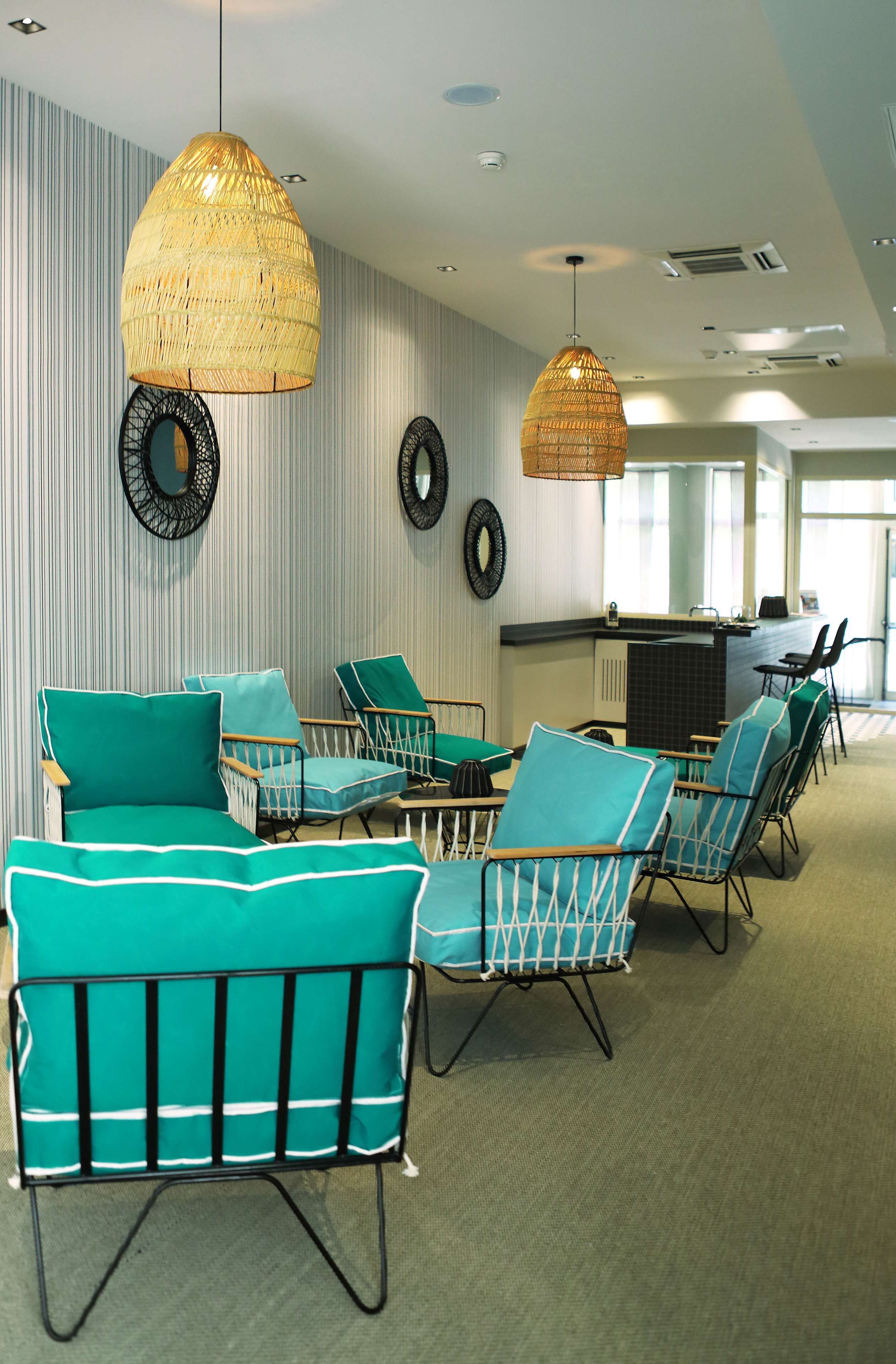 A modern lounge area with wicker pendant lighting, teal upholstered chairs, and a central table.