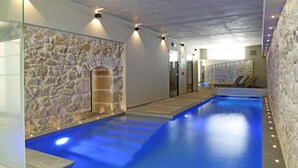 Une piscine intérieure moderne avec des murs en pierre et un éclairage encastré.