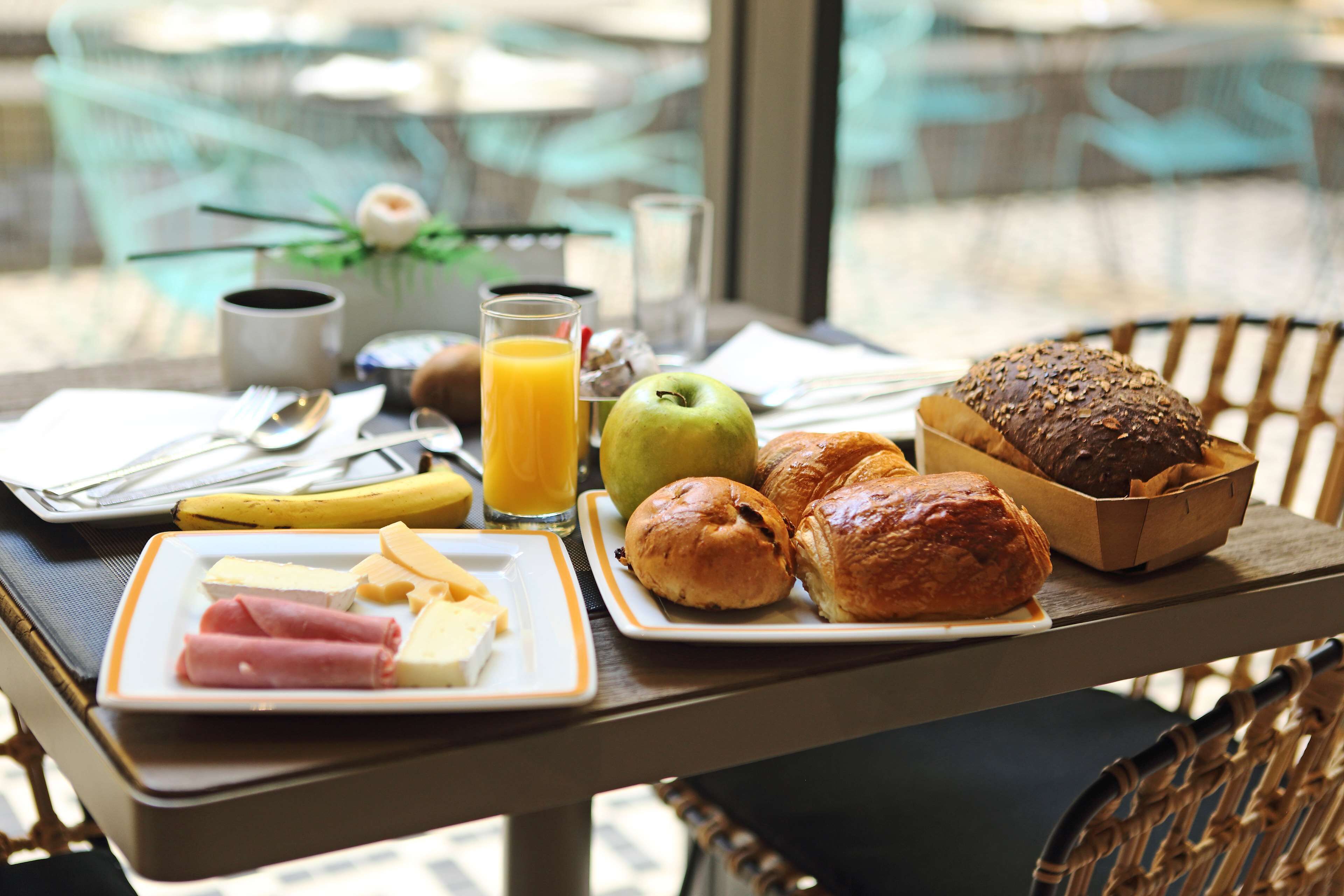 Una mesa de desayuno con platos de comida, un vaso de jugo de naranja y una cesta de pan.