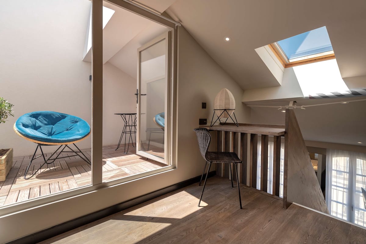 A modern loft bedroom with a skylight, a wooden staircase, and a view of the adjacent room.