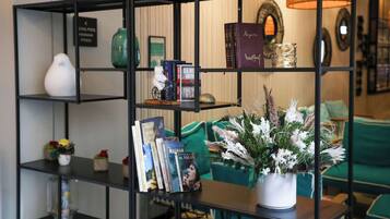 Une bibliothèque remplie de livres et d’objets décoratifs, un canapé vert et un vase avec des fleurs.