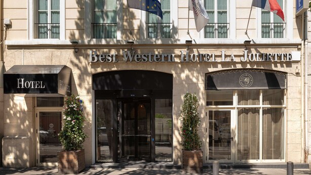 La façade de l’hôtel Best Western La Joliette, avec ses drapeaux, ses portes d’entrée et ses plantes en pot.