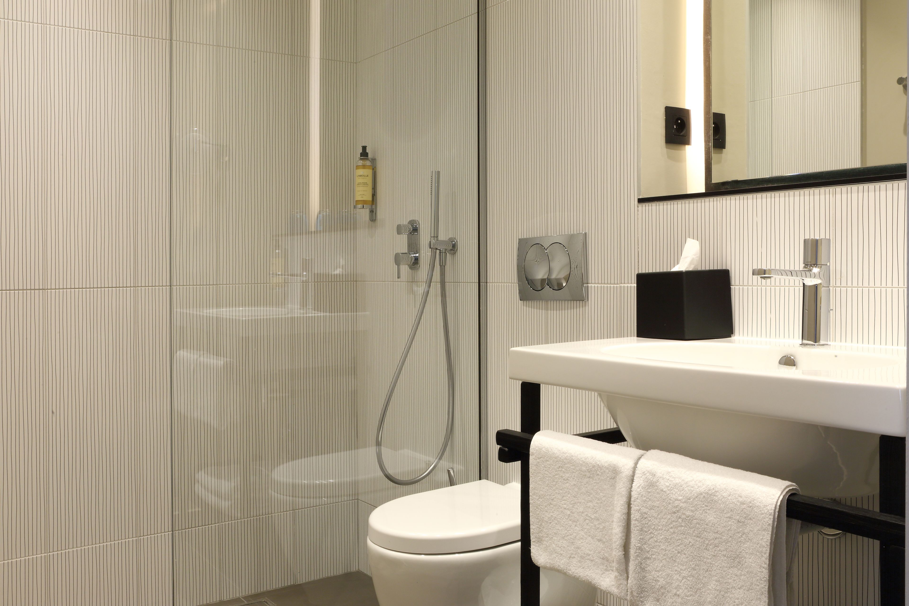 A modern bathroom with a toilet, a shower, and a sink with a towel rack.
