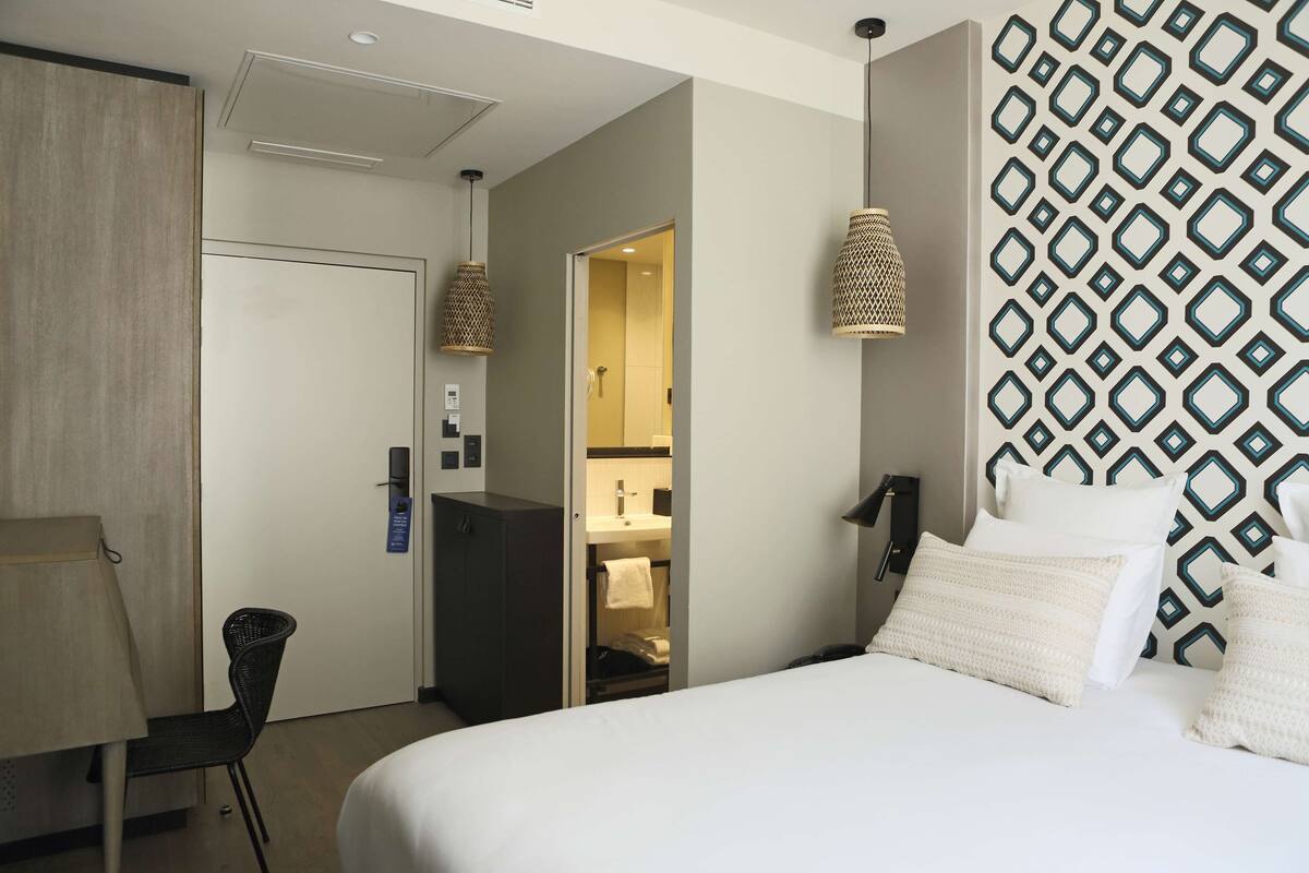 Een hotelkamer met een bed, een bureau, een stoel, een kledingkast en een badkamer die door een open deur zichtbaar is.