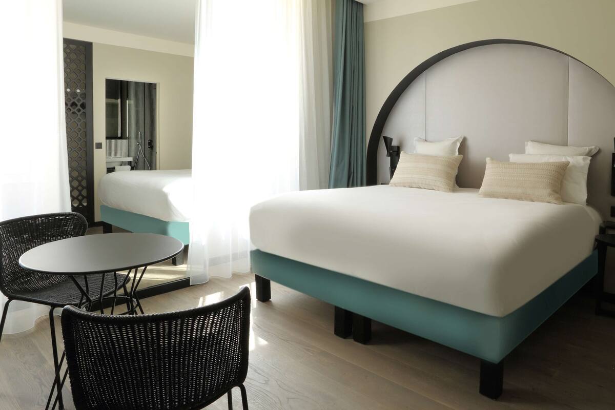 Een hotelkamer met een groot bed, een ronde tafel, twee stoelen en uitzicht op de gang.