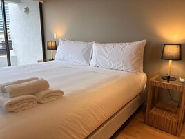 Habitación de hotel con una cama grande, dos lámparas de noche, una mesita de noche y una ventana con vistas a edificios.