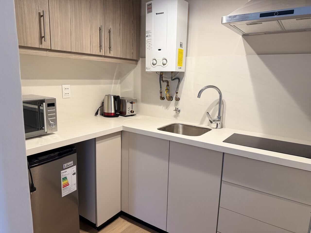 Una cocina compacta con lavavajillas integrado, microondas, pileta y calentador de agua.