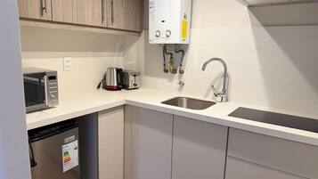 Una cocina compacta con lavavajillas integrado, microondas, pileta y calentador de agua.