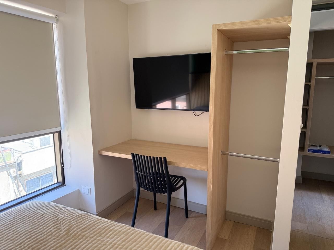 A room with a bed, a desk with a chair, a TV mounted on the wall, and a closet.