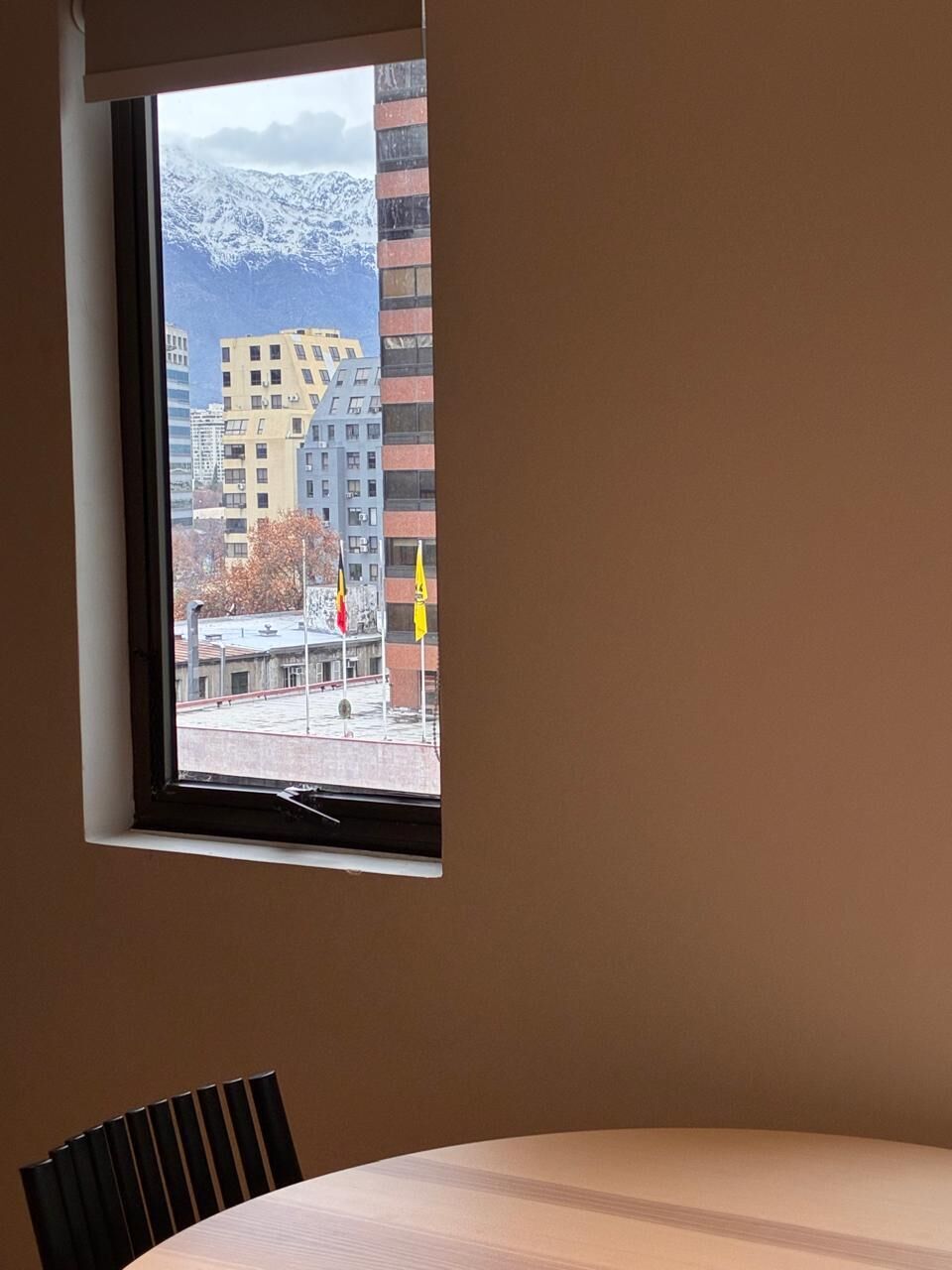 A room with a window overlooking a snowy mountain and buildings.