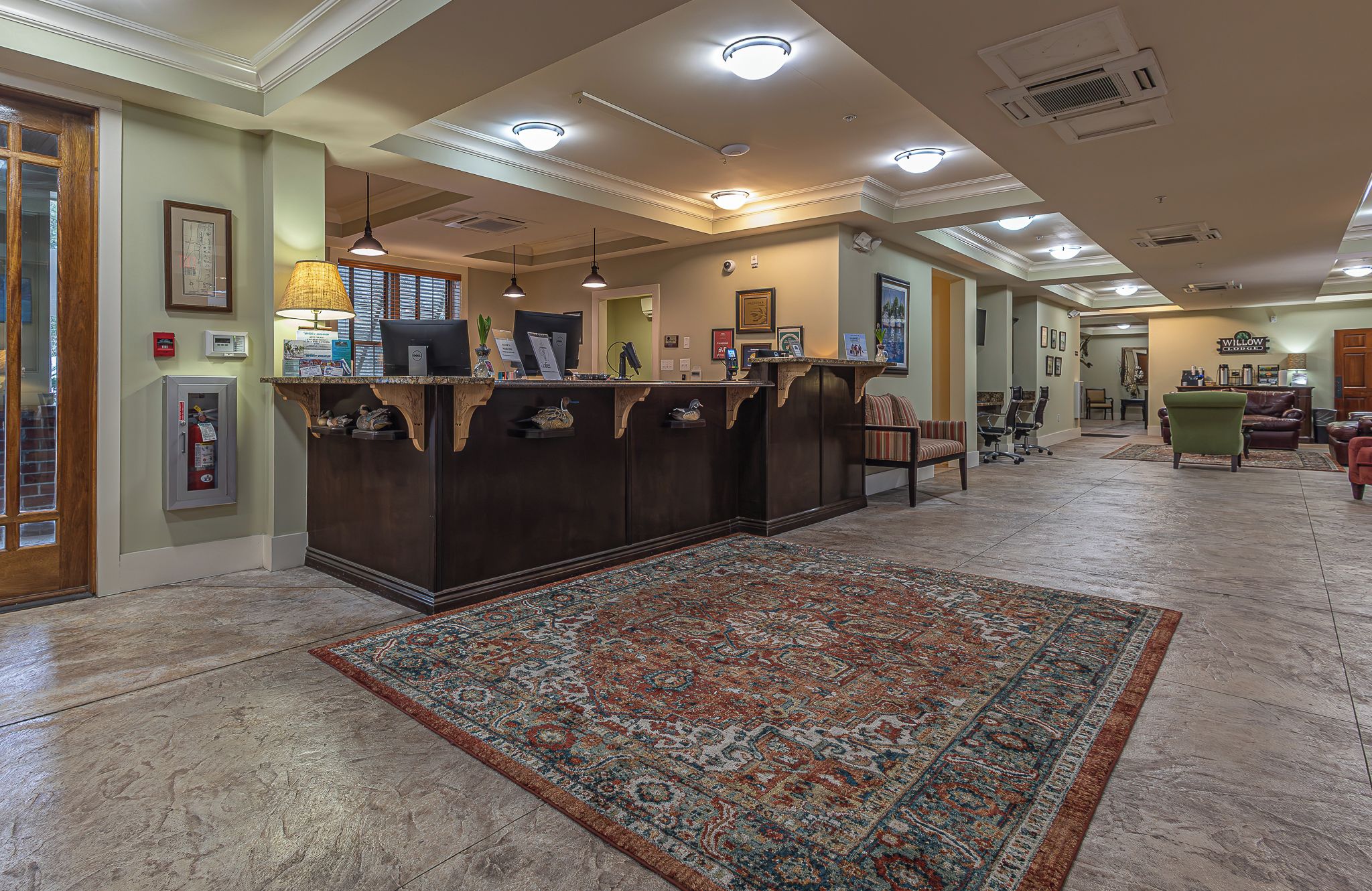 A reception area with a reception desk, a patterned rug, and a hallway leading to a seating area.