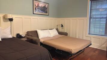 A hotel room with two beds, a desk, a lamp, a phone, and a window with blinds.
