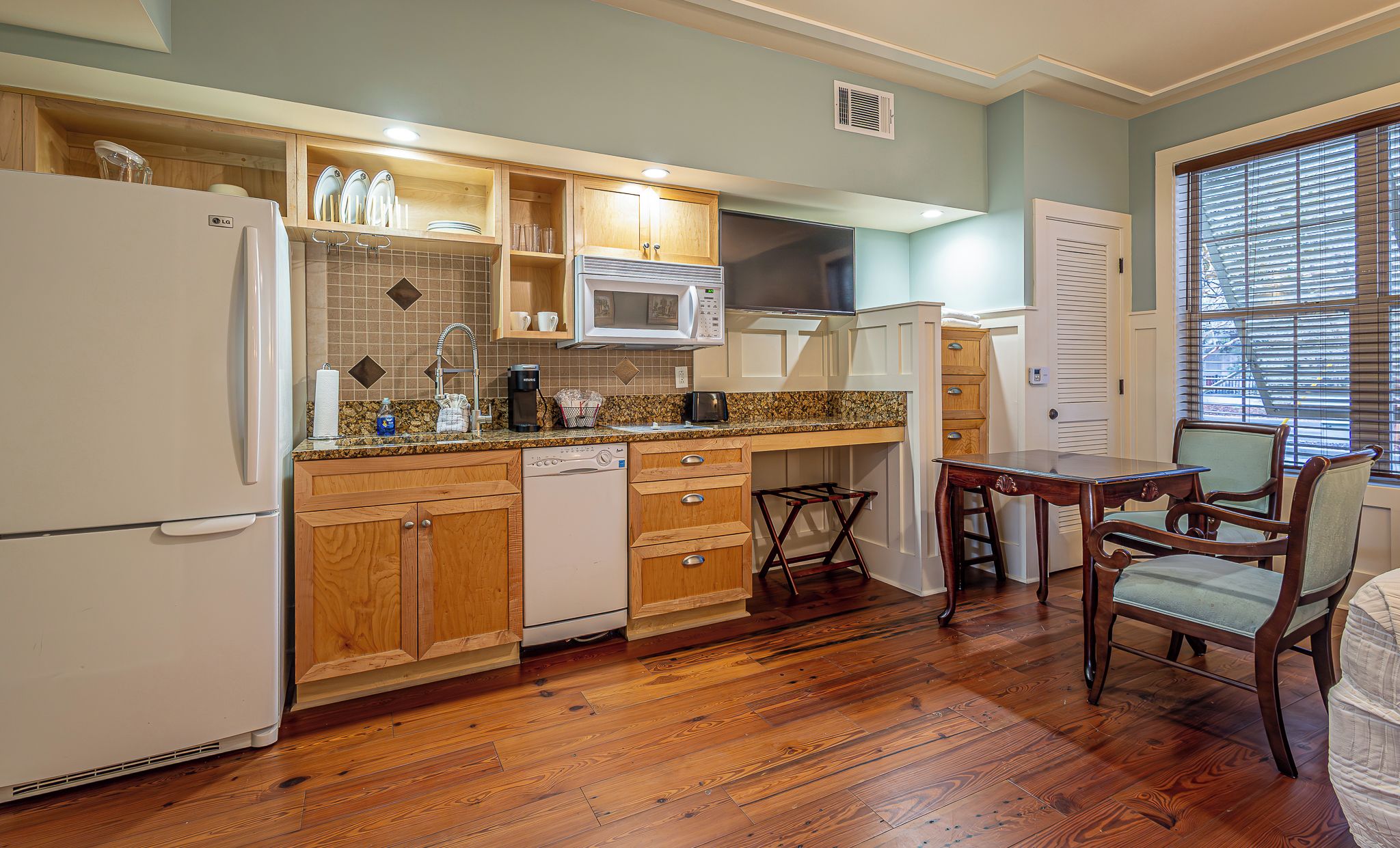 A kitchen with wooden cabinets, a microwave, a refrigerator, and a dining area with a table and chairs.