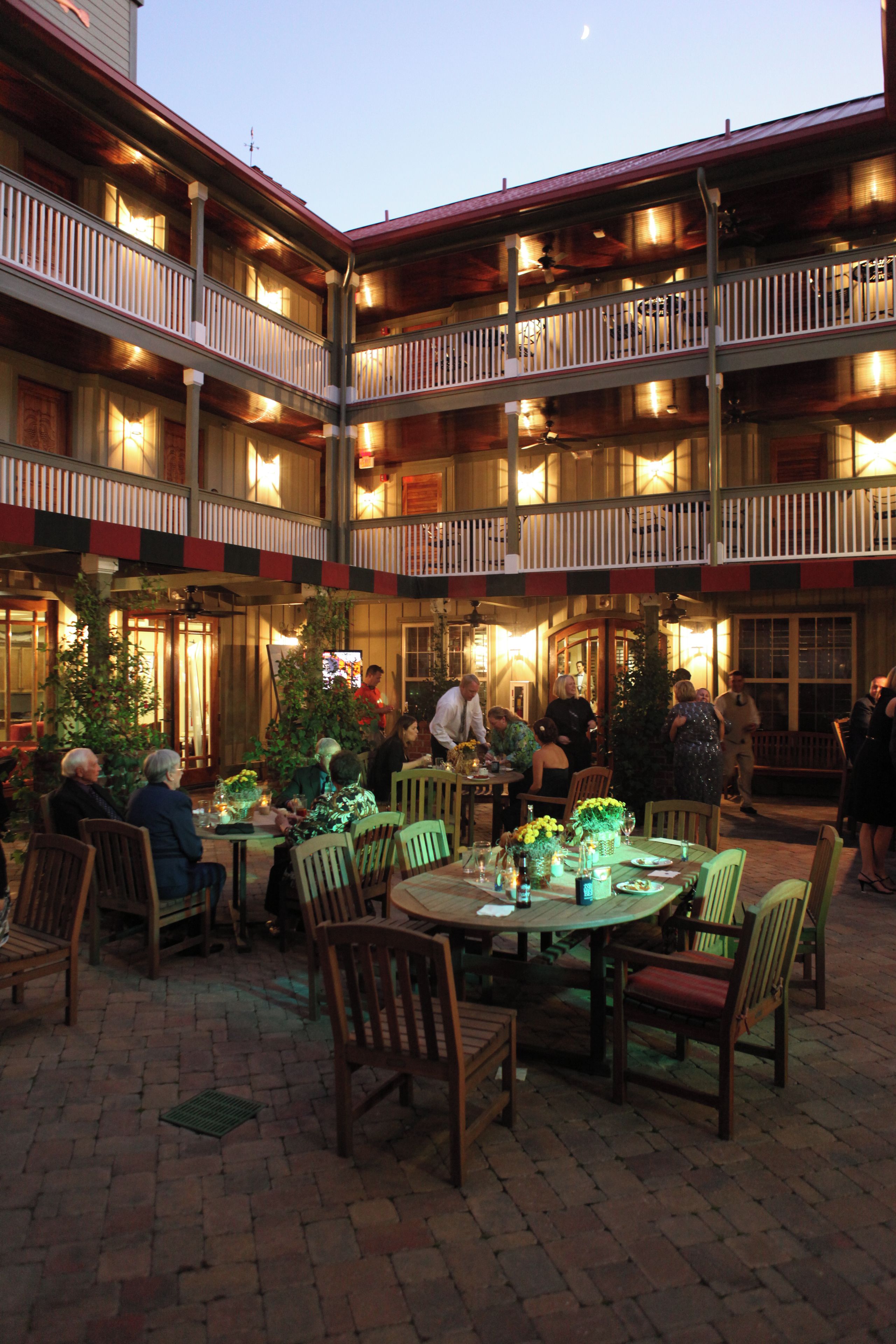 A multi-story building with outdoor dining areas, multiple balconies, and a brick floor.