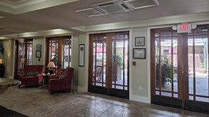 A lobby with a reception desk, two red armchairs, a table with a lamp, and a large glass door leading outside. - Willow Lodge (Murrells Inlet)