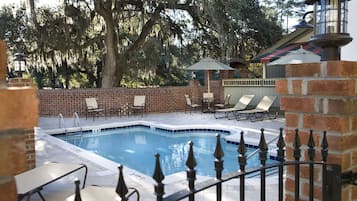 Relax by the serene pool surrounded by lush trees and a brick wall, with lounge chairs and umbrellas for a tranquil retreat.