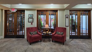 A lobby with two red armchairs, a small table with a lamp, and a view through a glass door. - Willow Lodge (Murrells Inlet)