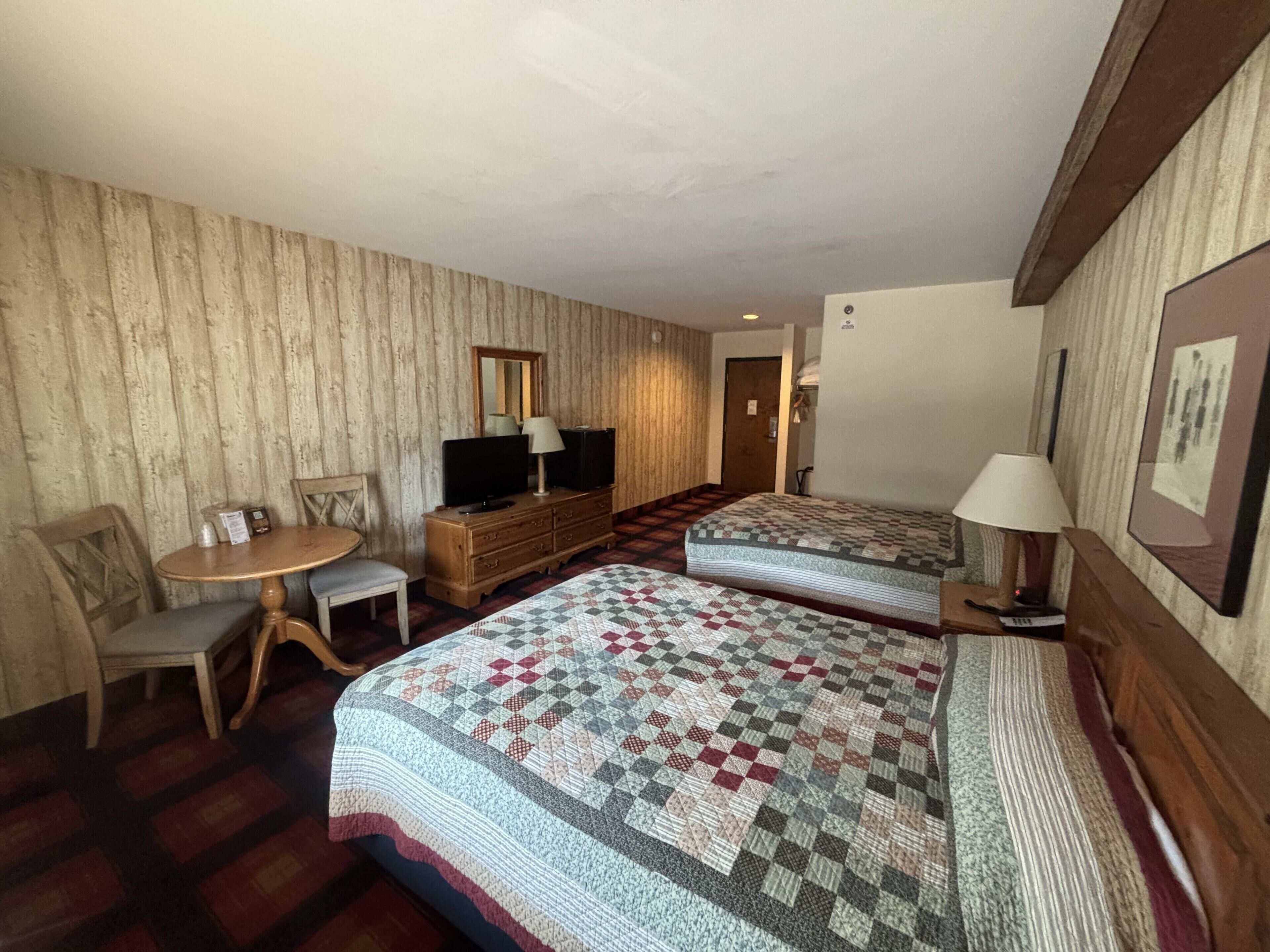 A hotel room with a bed, a desk, a chair, a dresser, a television, and a mirror.