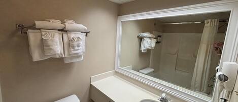 A bathroom with a toilet, sink, and mirror. There are towels hanging on a rack.