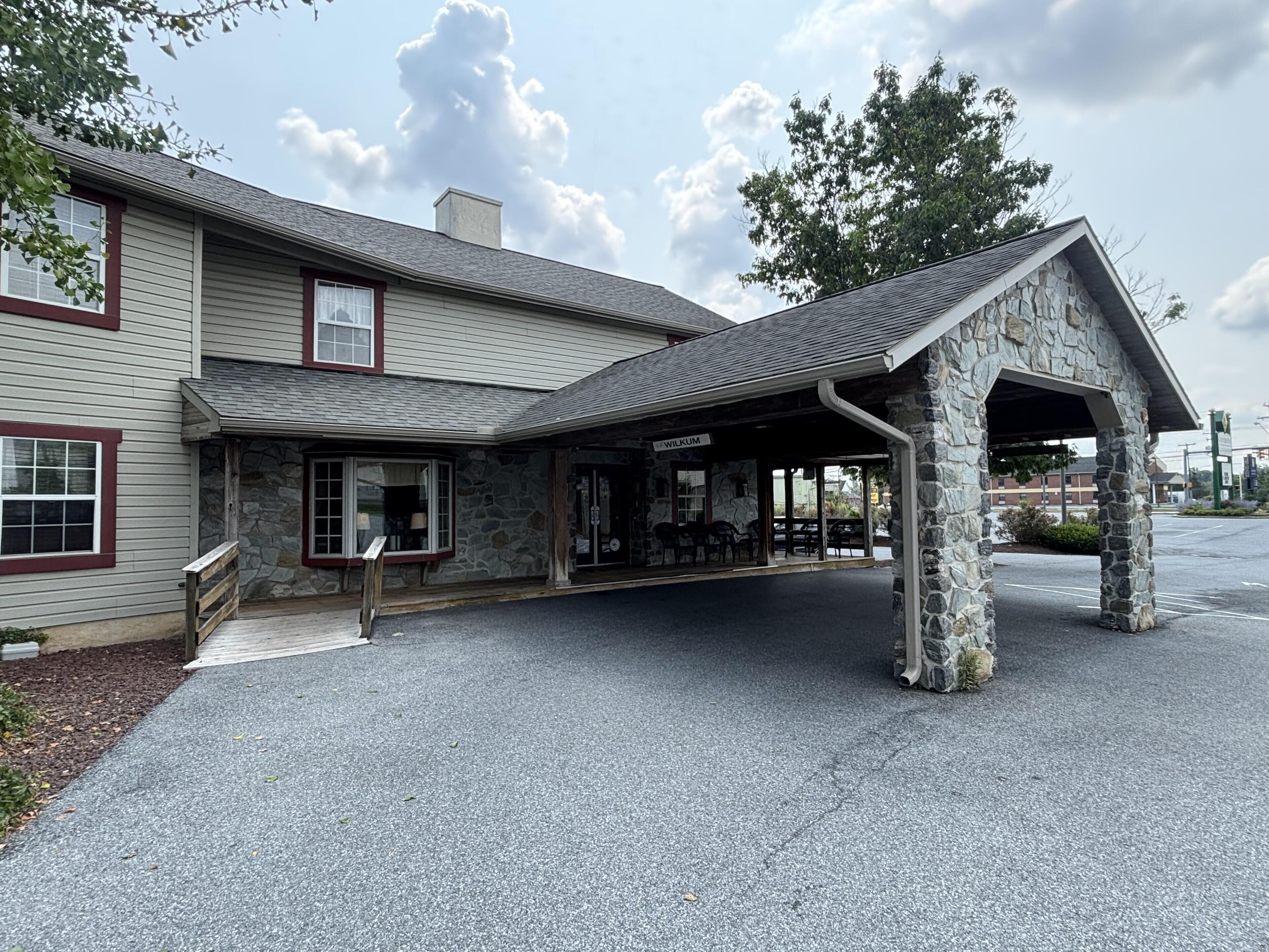 A building with a stone facade, a covered outdoor seating area, and a sign that reads 'WILKUM.'