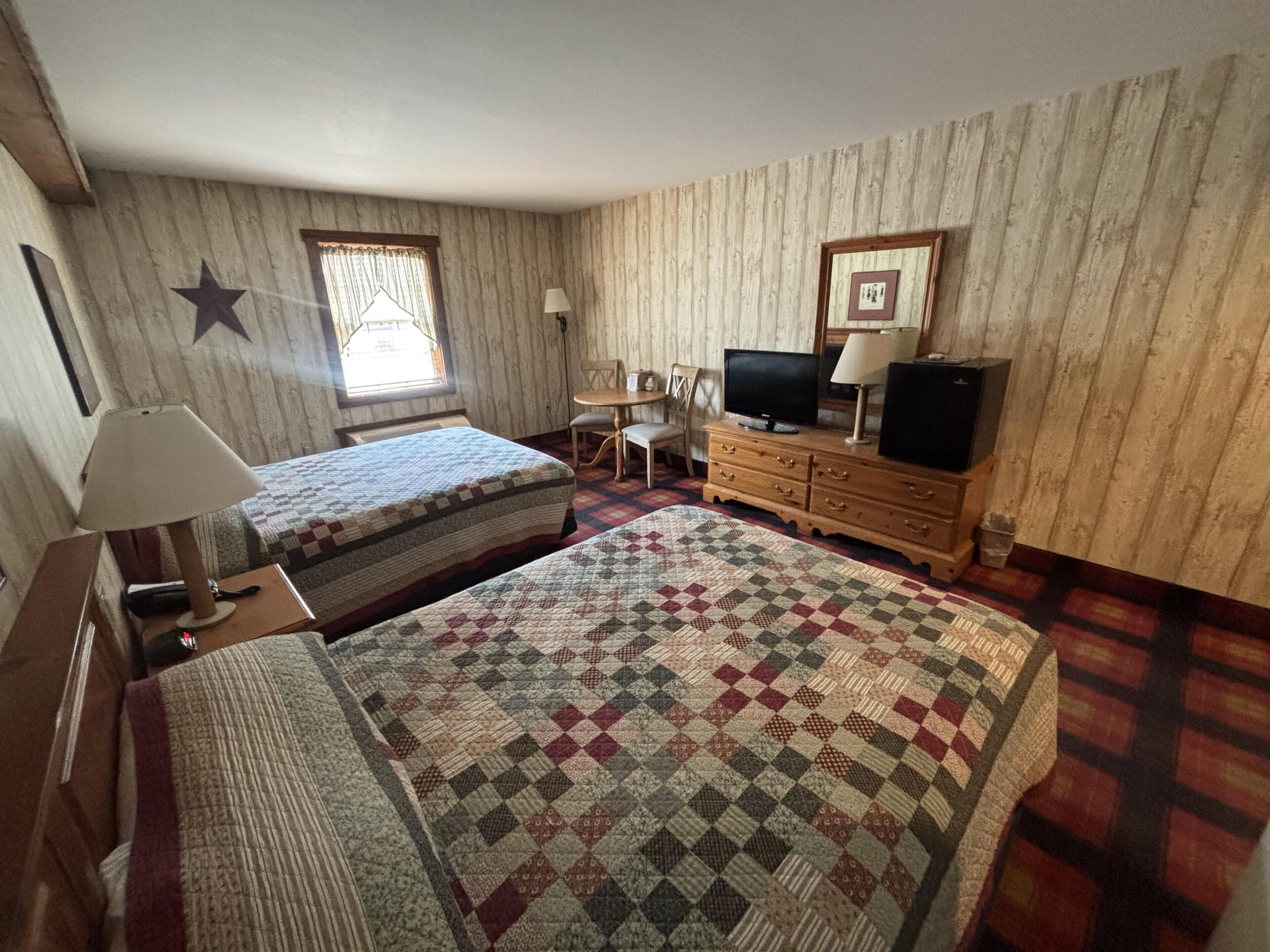 A room with two beds, a television, a desk, and a chair.