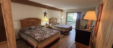A room with two wooden beds, a star decoration on the wall, a desk with a lamp, and a view of the outdoors through a window.