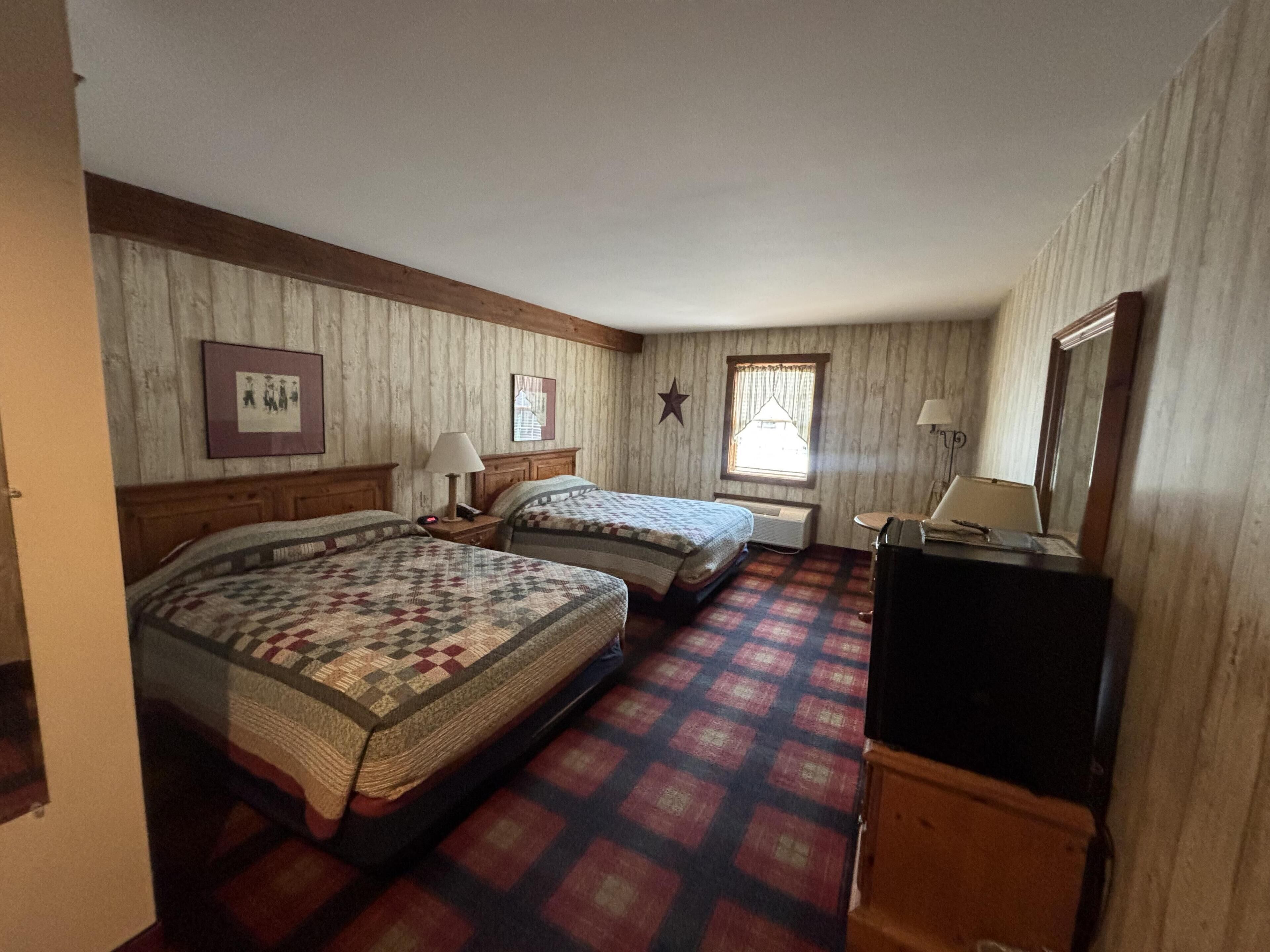A room with two beds, a desk, a mirror, and a window with curtains.