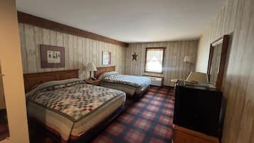 A room with two beds, a desk, a mirror, and a window with curtains.