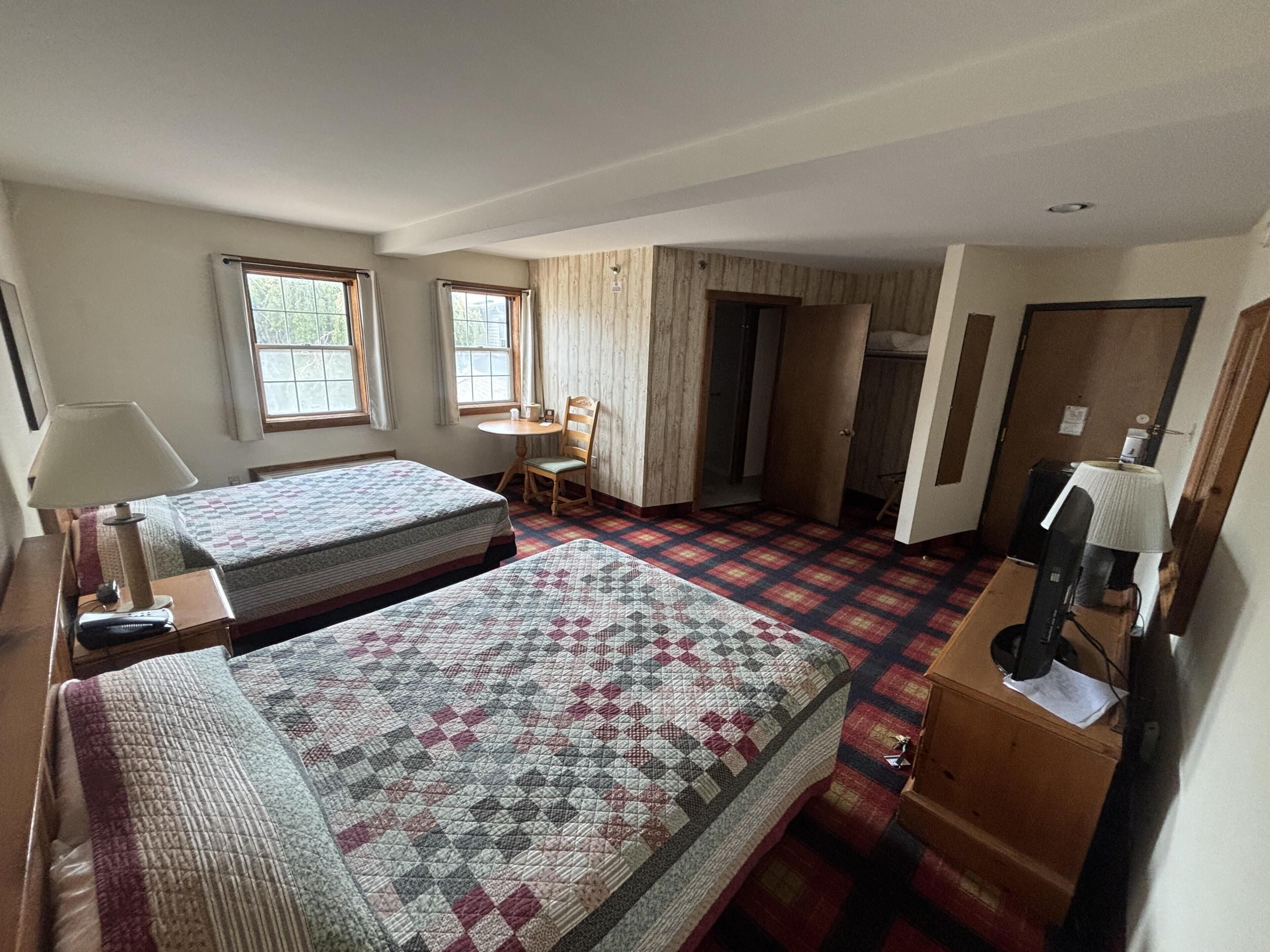 Habitación de hotel con dos camas, un escritorio, una silla y un televisor.