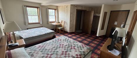 Habitación de hotel con dos camas, un escritorio, una silla y un televisor.