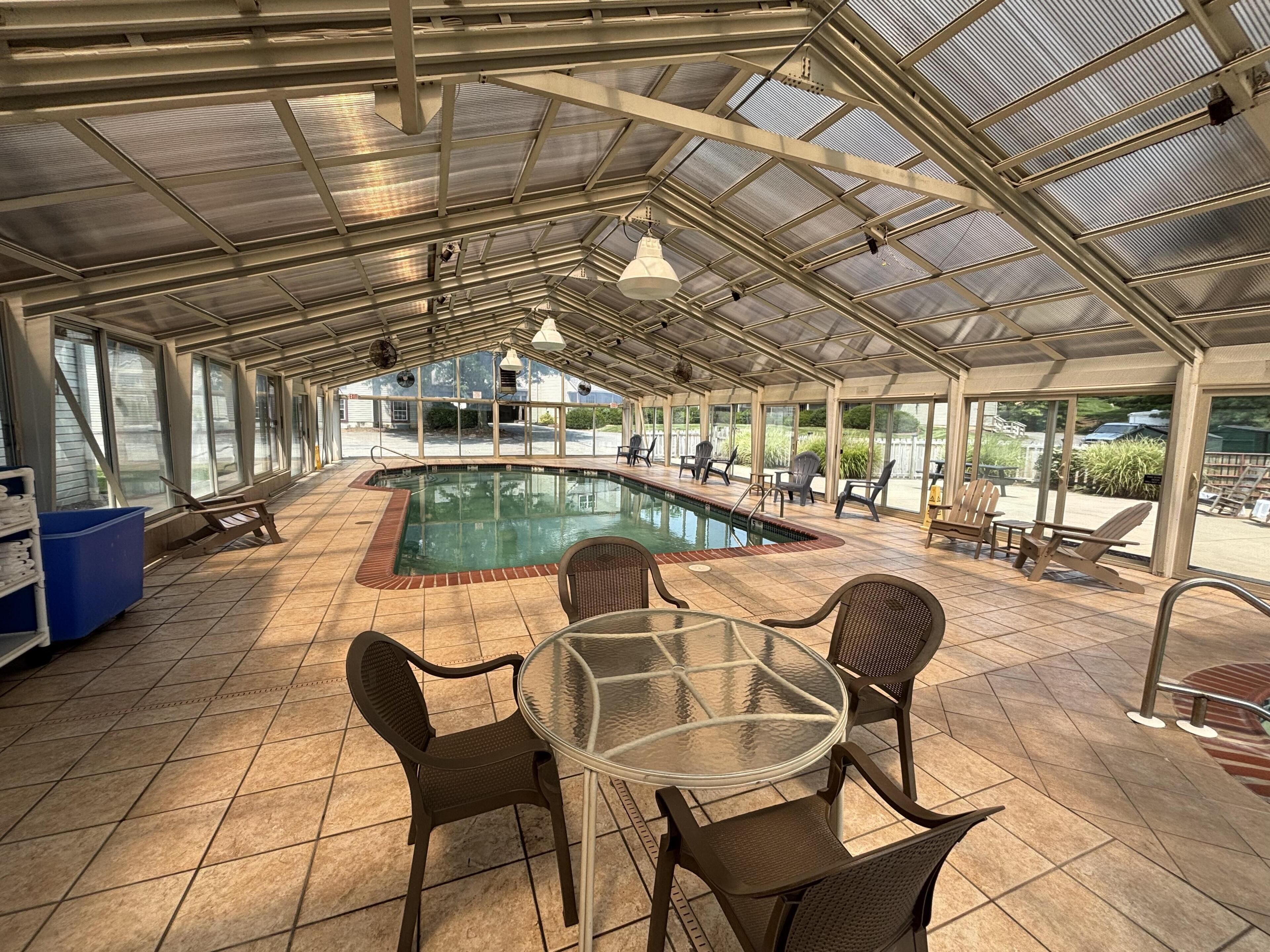An indoor swimming pool with a glass table and chairs, surrounded by a covered patio area.