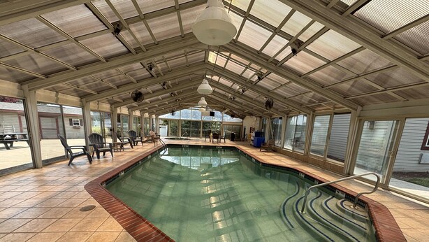 Une piscine intérieure, dotée d’un sol carrelé, d’un espace aménagé avec des chaises autour du bassin, et offrant une vue à travers de grandes fenêtres.